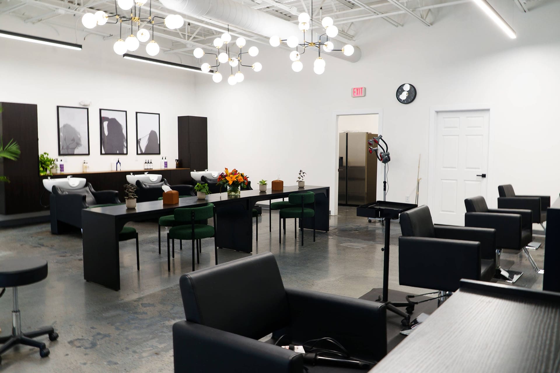 The open salon floor under globe chandeliers, with a long table and black styling chairs