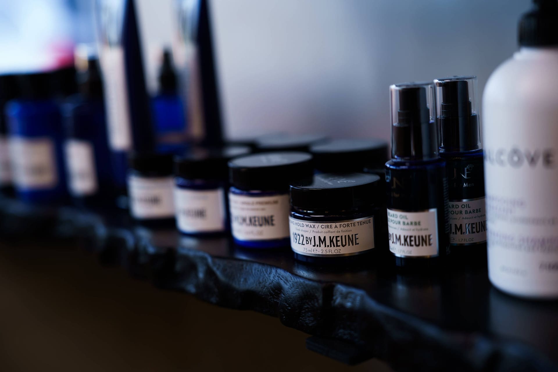Dark tins and small bottles of grooming products on a black shelf