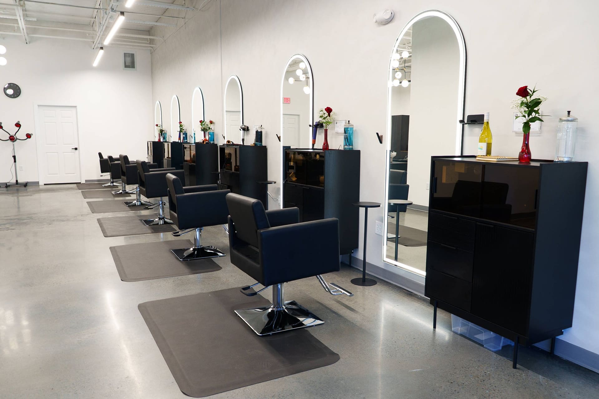 Styling stations along the white wall, each with an arch mirror and a black chair