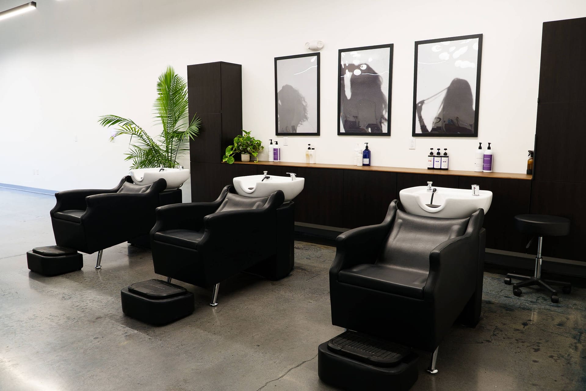 Three black shampoo chairs with white bowls under framed black-and-white prints